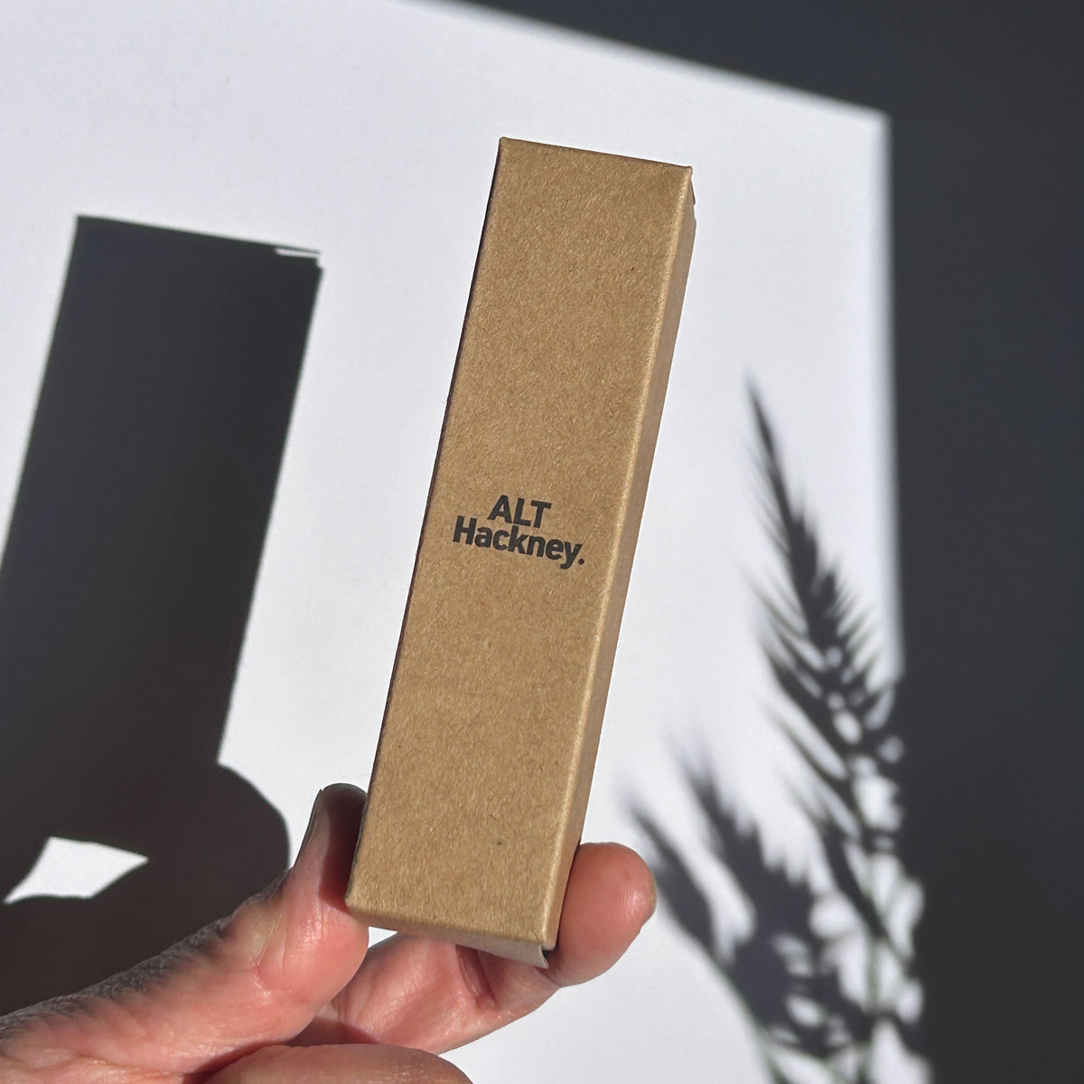 Hand holding a brown eco box with 'ALT Hackney.' branding against a light background