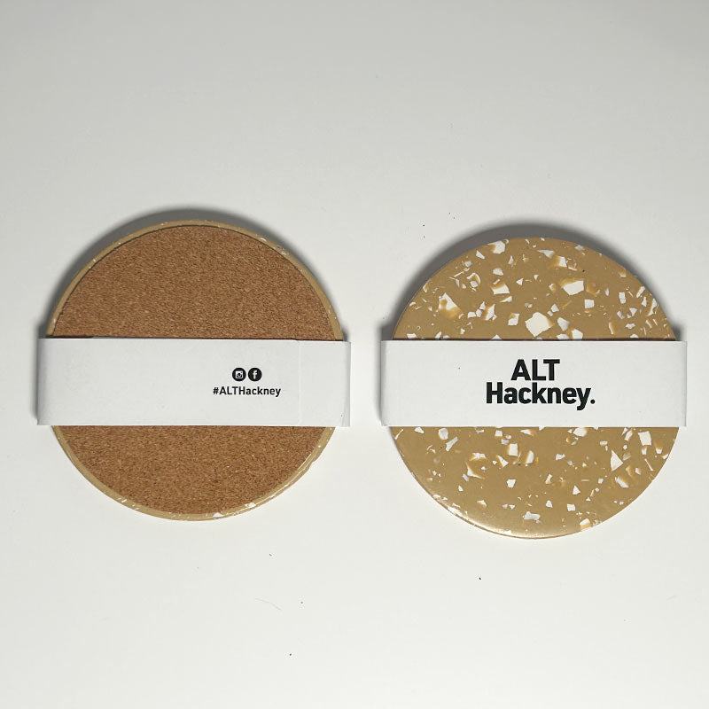 Two round coasters side by side on a white background. The left coaster has a brown cork backing with a white paper band reading '#ALTHackney'.