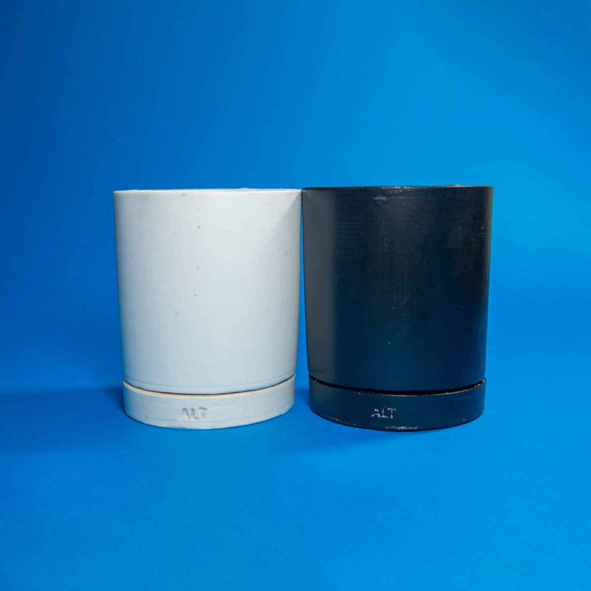 Two cylindrical containers, one white and one black, on a blue background.