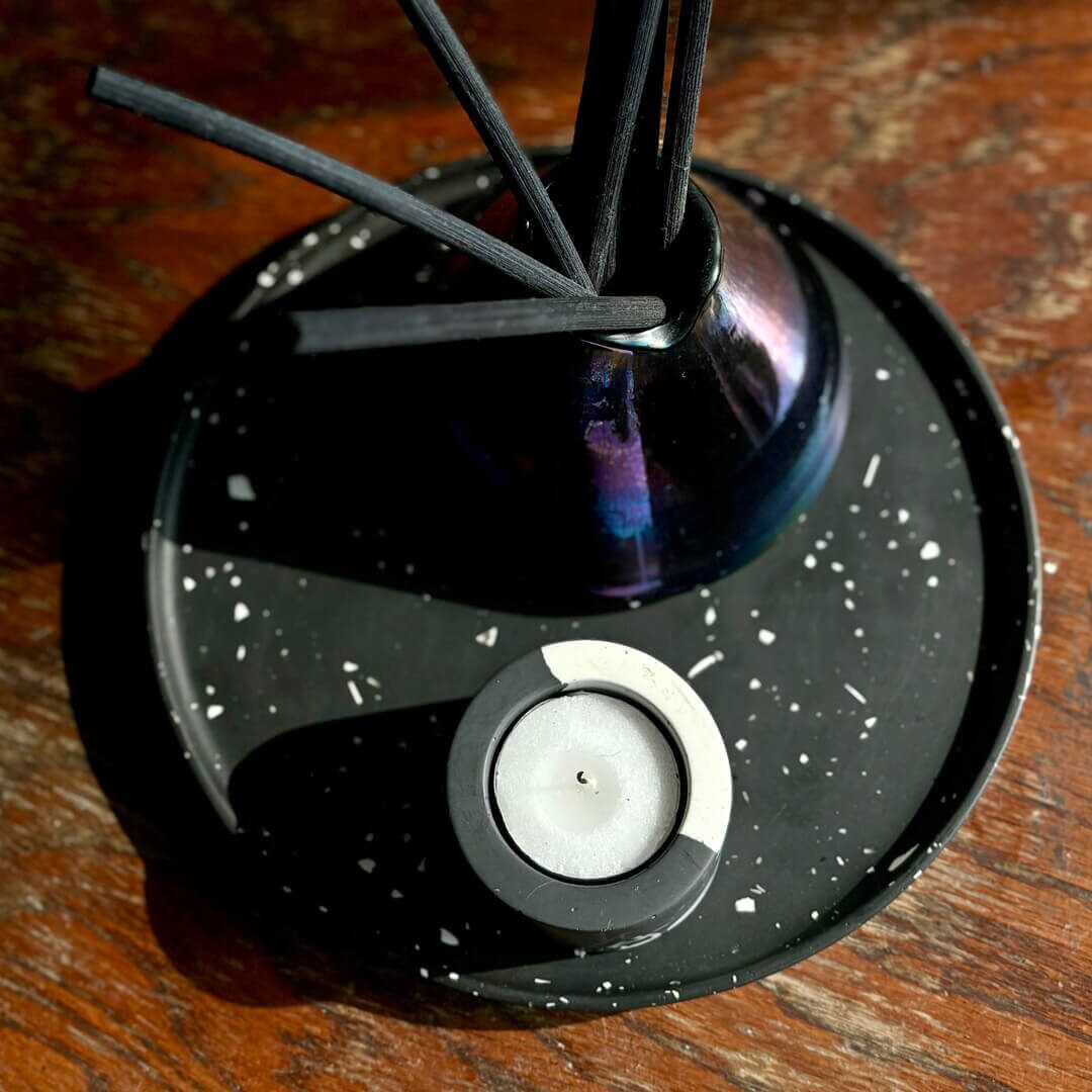A diffuser with reeds and a grey and white marble candle holder on a wooden surface