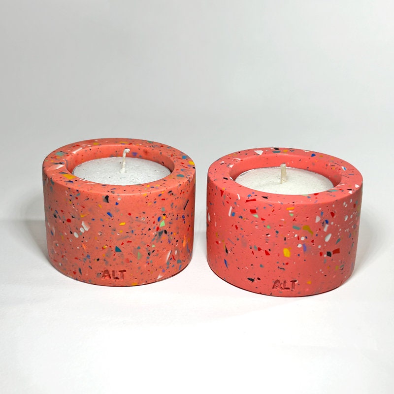 Two pink with rainbow confetti terrazzo-patterned tealight candle holders with white candles on a light gray background.