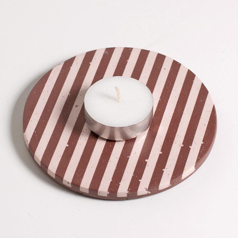 A tea light on a burgundy and light pink checkered coaster on a white background