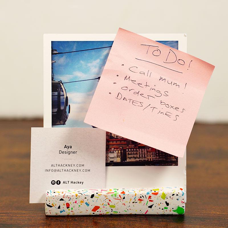 A post card with a pink 'To Do' list, business card, and colourful photo holder on a wooden surface.