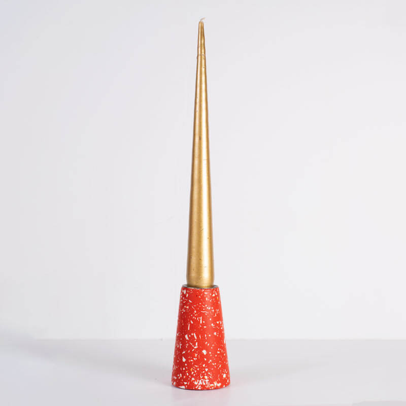A decorative cone-shaped red terrazzo taper candle holder with a metallic gold pointed taper candle set against a plain white background.