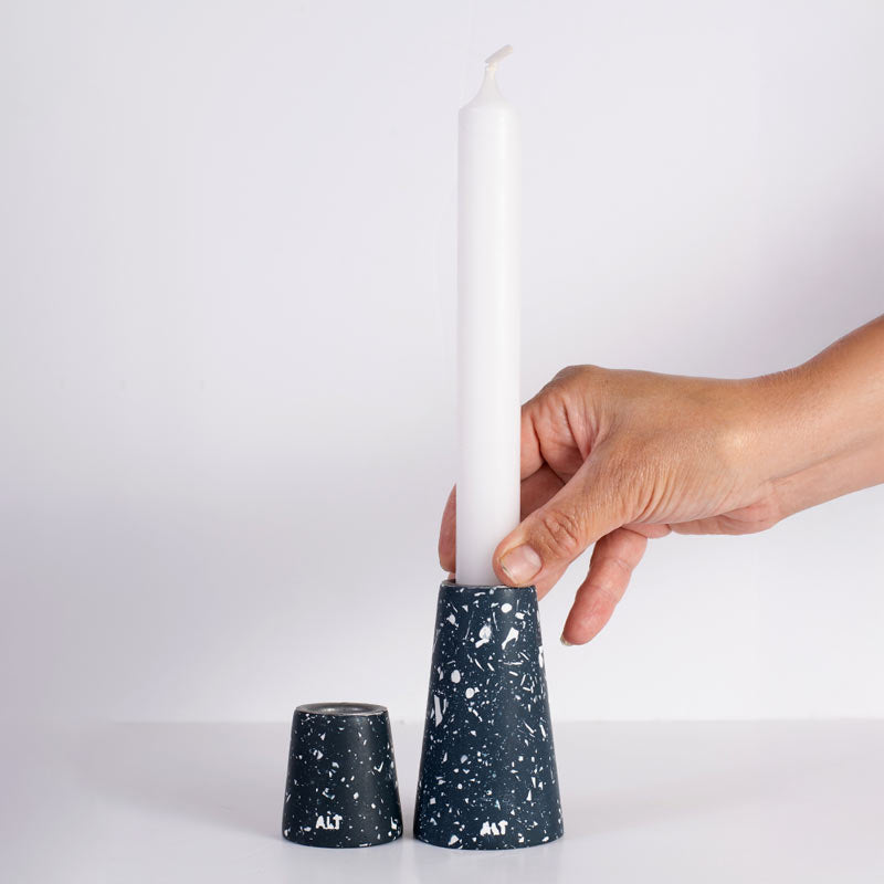 A hand inserts a white taper candle into a navy blue and white terrazzo taper candle holder, with the matching holder cap placed beside it on a clean white background.