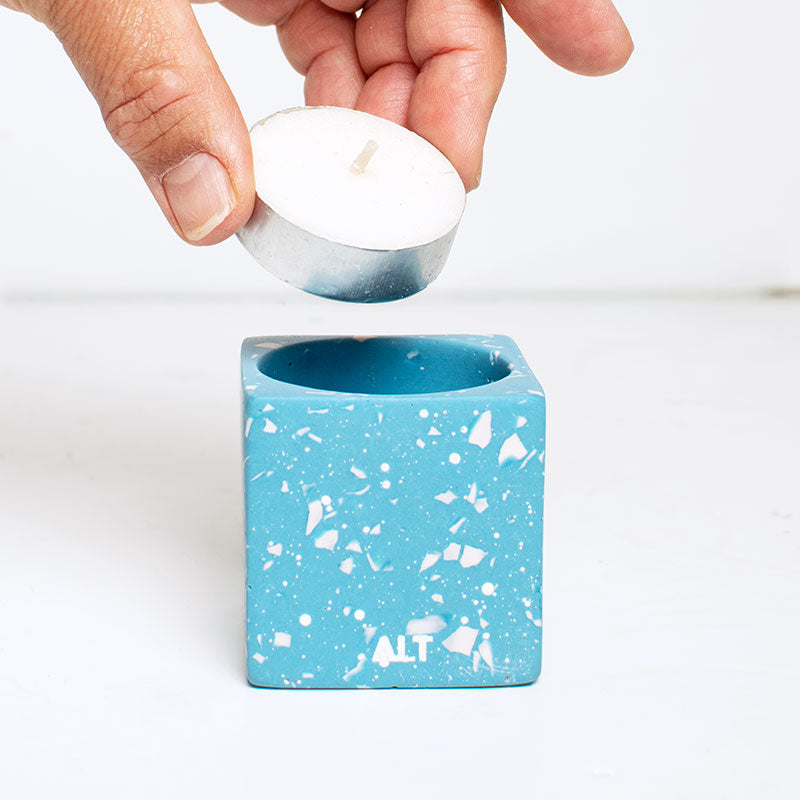 Hand placing a tea light into a light blue speckled candle holder with 'ALT' branding.