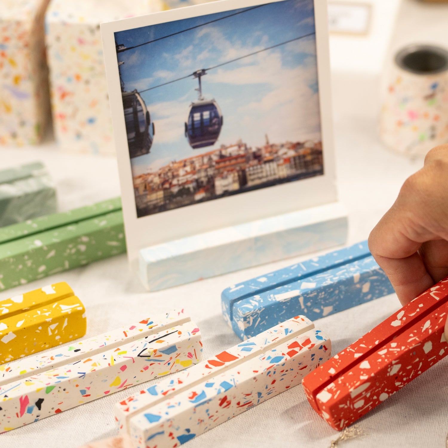 ALT Hackney terrazzo photo holders in assorted colours—yellow, blue, green and red—displaying a small printed photograph of cable cars over a city skyline.