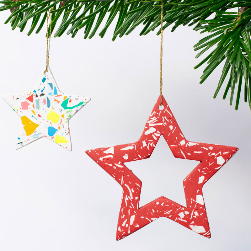 A small rainbow terrazzo star and a large red and white terrazzo star Christmas decoration hung on a Christmas tree branch