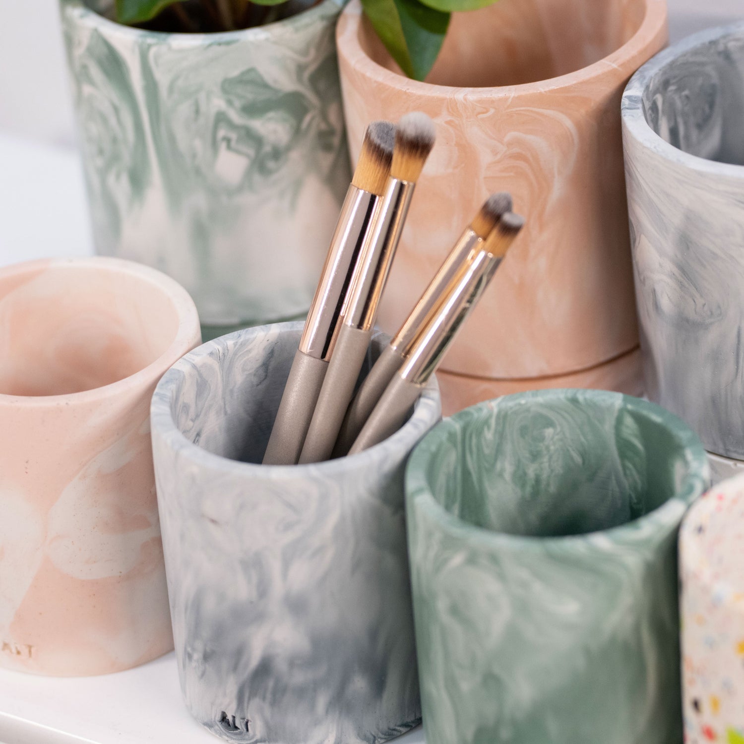 ALT text: Various marble pen pots and plant pots in navy, moss green, and salmon pink, displayed together as a coordinated set