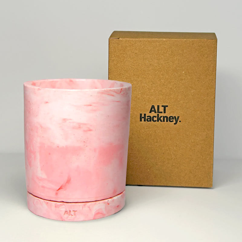 Pink marbled cylindrical plant pot with a drainage and a water tray  with a cardboard box labeled 'ALT Hackney' on a gray background