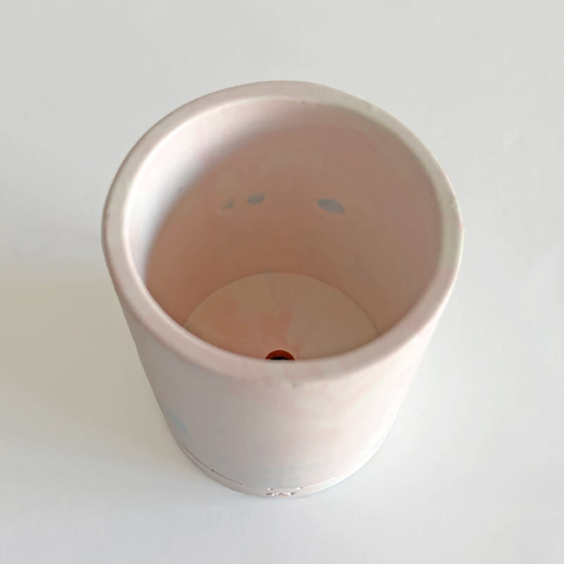 Jesmonite planter with marbled design with a drainage hole and a water tray on a light surface