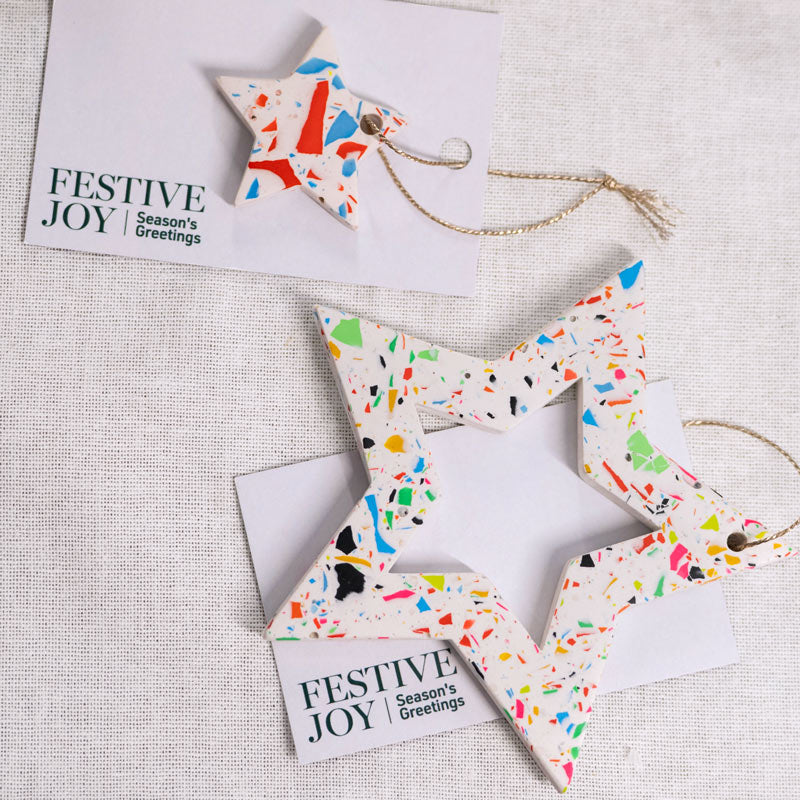 Rainbow terrazzo star-shaped Christmas ornaments with 'Festive Joy' cards on a textured surface