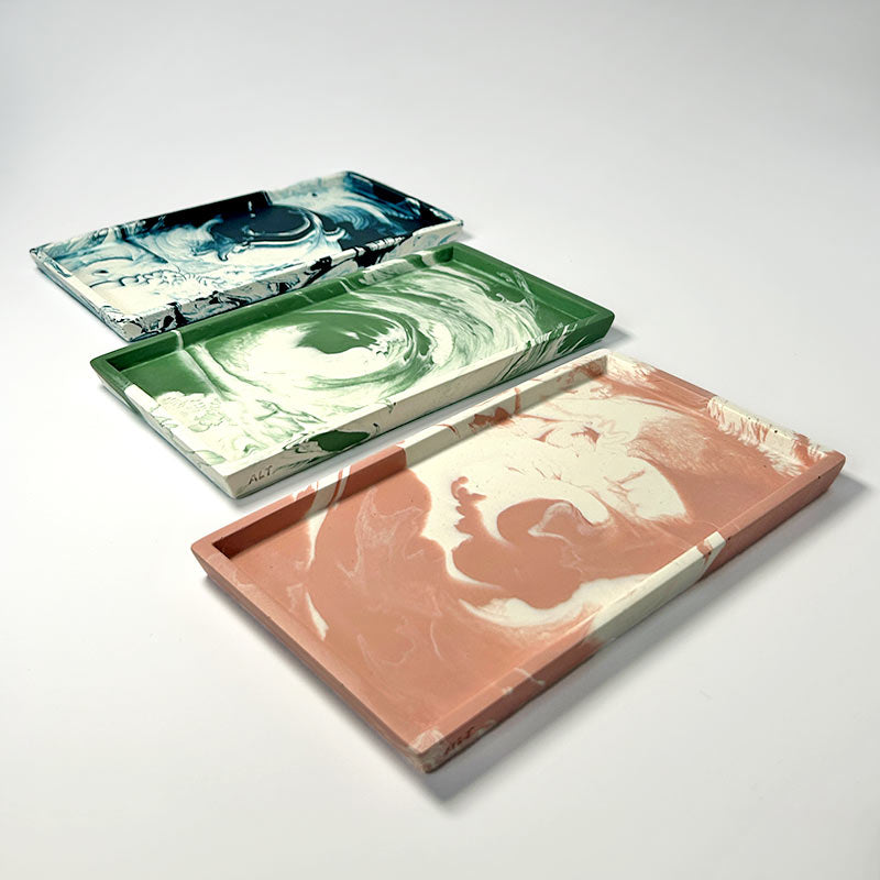 Three marbled decorative trays in moss green, salmon pink, and navy on a light grey background
