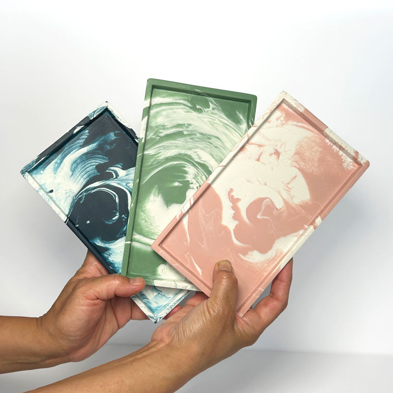 Three colourful rectangular small marbled trays held by hands against a white background
