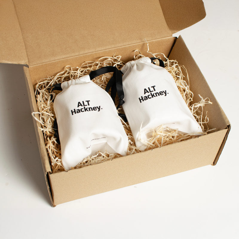 Two white drawstring bags with 'ALT Hackney' logo in a cardboard box