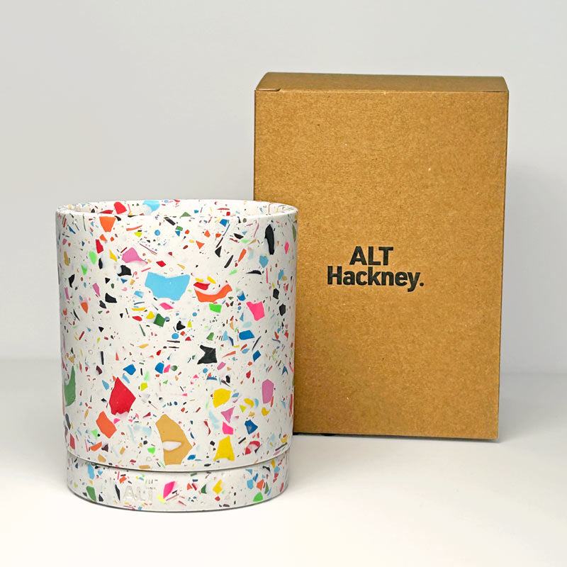 Colourful terrazzo-patterned plant pot with drainage hole and a separate water tray next to a brown box with 'ALT Hackney' branding on a light gray background