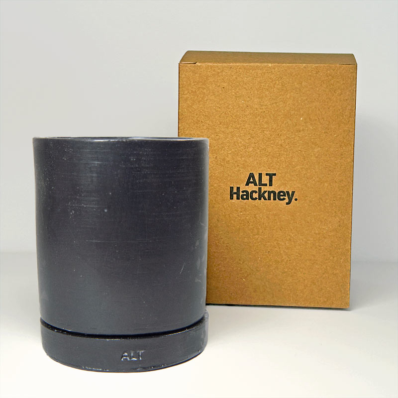 Black Jesmonite planter with 'ALT Hackney' branding next to a brown box on a gray background