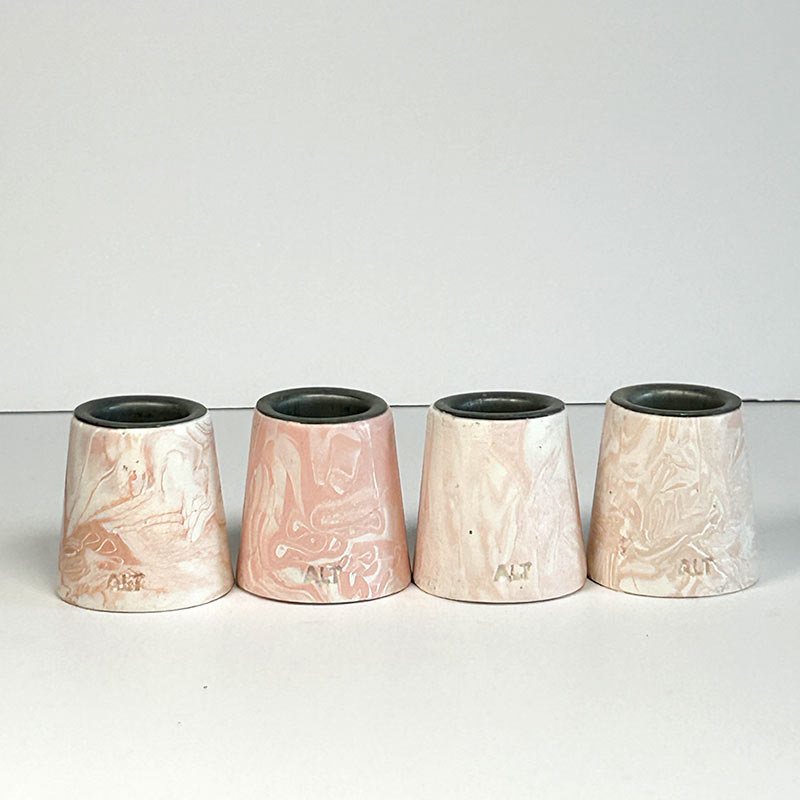 Four small tapered candle holders with a salmon pink and white marbled pattern, arranged in a row against a plain light gray background.