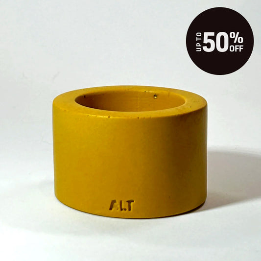 A mustard yellow tea light candle holder, featuring the embossed letters 'ALT' near the bottom, set against a plain white background with a black 'Up to 50% OFF' promotional badge in the top right corner.