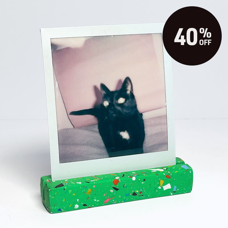 A green with rainbow speckled photo holder displaying a square instant photograph of a black cat, set against a plain white background with a black circular '40% OFF' promotional badge in the top right corner.