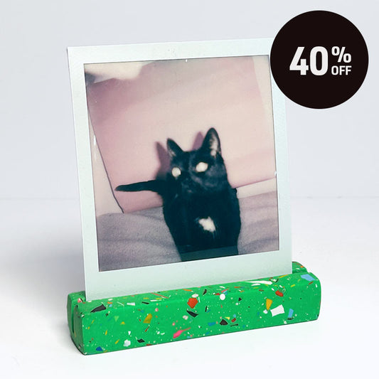 A green with rainbow speckled photo holder displaying a square instant photograph of a black cat, set against a plain white background with a black circular '40% OFF' promotional badge in the top right corner.