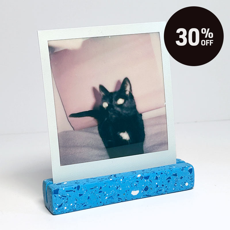 A blue speckled photo holder displaying a square instant photograph of a black cat, set against a plain white background with a black circular '30% OFF' promotional badge in the top right corner.
