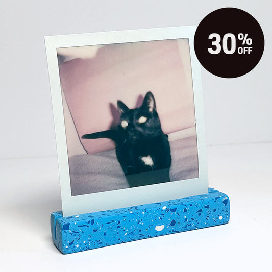 A blue speckled photo holder displaying a square instant photograph of a black cat, set against a plain white background with a black circular '30% OFF' promotional badge in the top right corner.