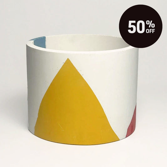 A cylindrical planter with a white base decorated with a large mustard yellow triangle and small accents of blue and red, shown on a neutral gray background with a '50% OFF' promotional sticker in the top right corner.