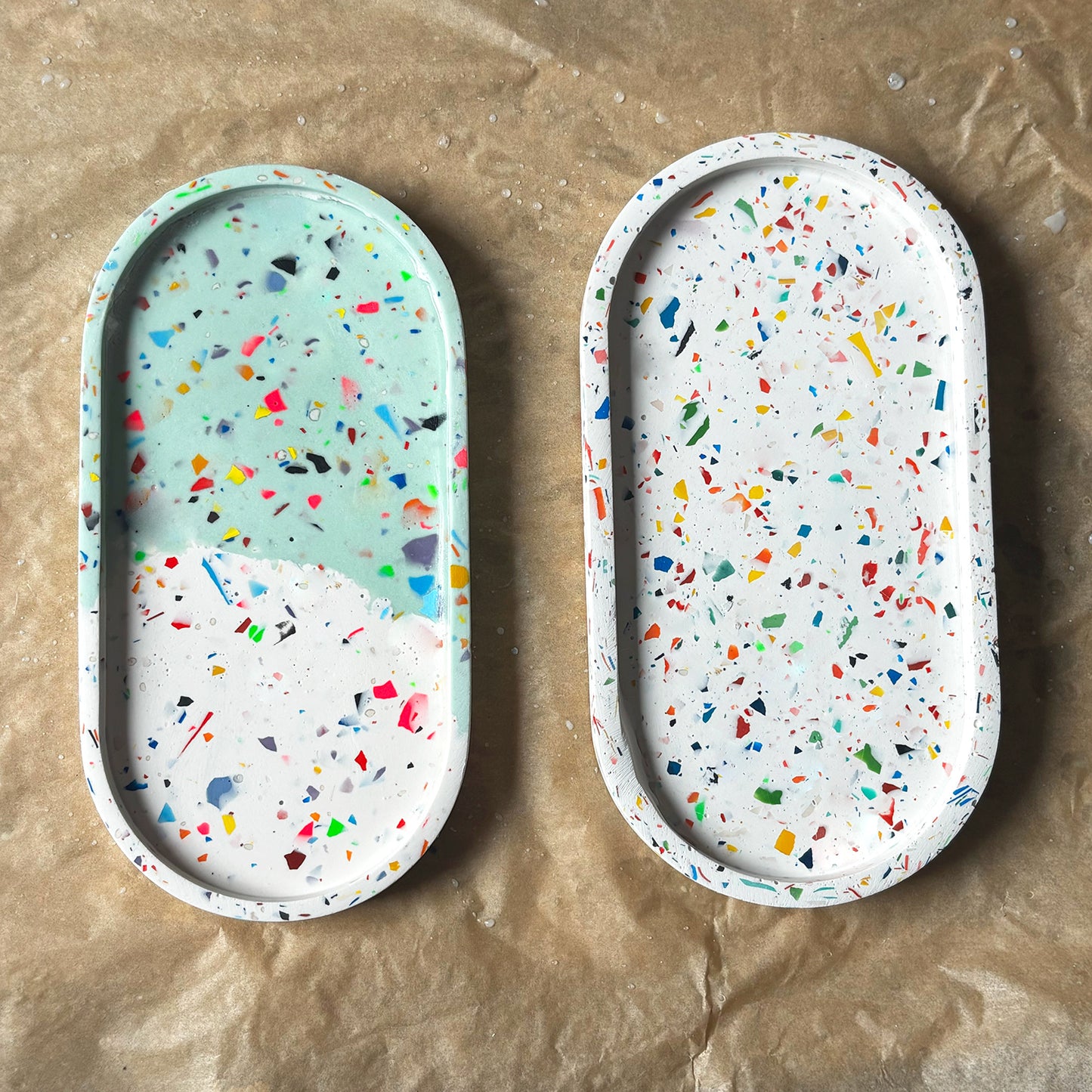 Two rainbow terrazzo oval trays on a brown surface