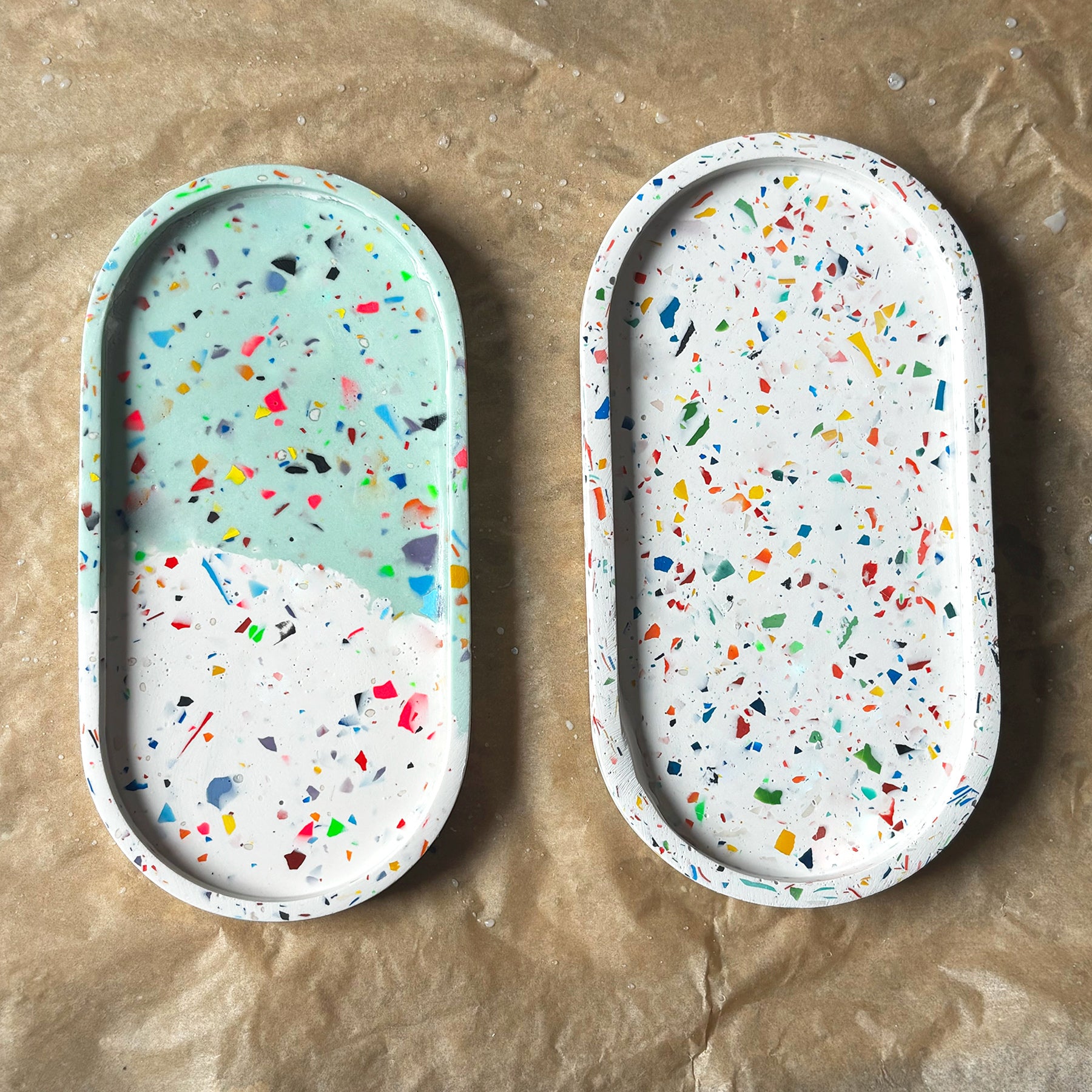 Two rainbow terrazzo oval trays on a brown surface