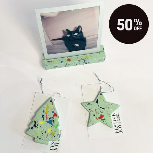 Three light mint green holiday ornaments with multicolor confetti-like speckles are displayed on a white background. One ornament is shaped like a photo frame holding a black cat, while the other two are star and tree shapes with silver hanging loops.