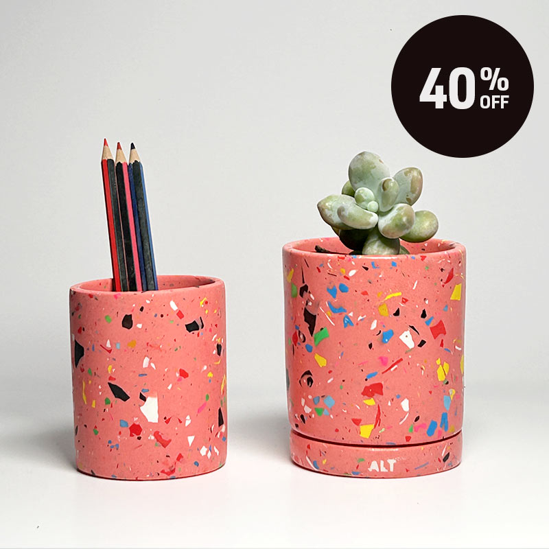 Two terrazzo-style pink desk accessories on a light gray background: a pencil holder with coloured pencils on the left and a small succulent planter on the right. A black circular badge in the top right reads '40% OFF'.
