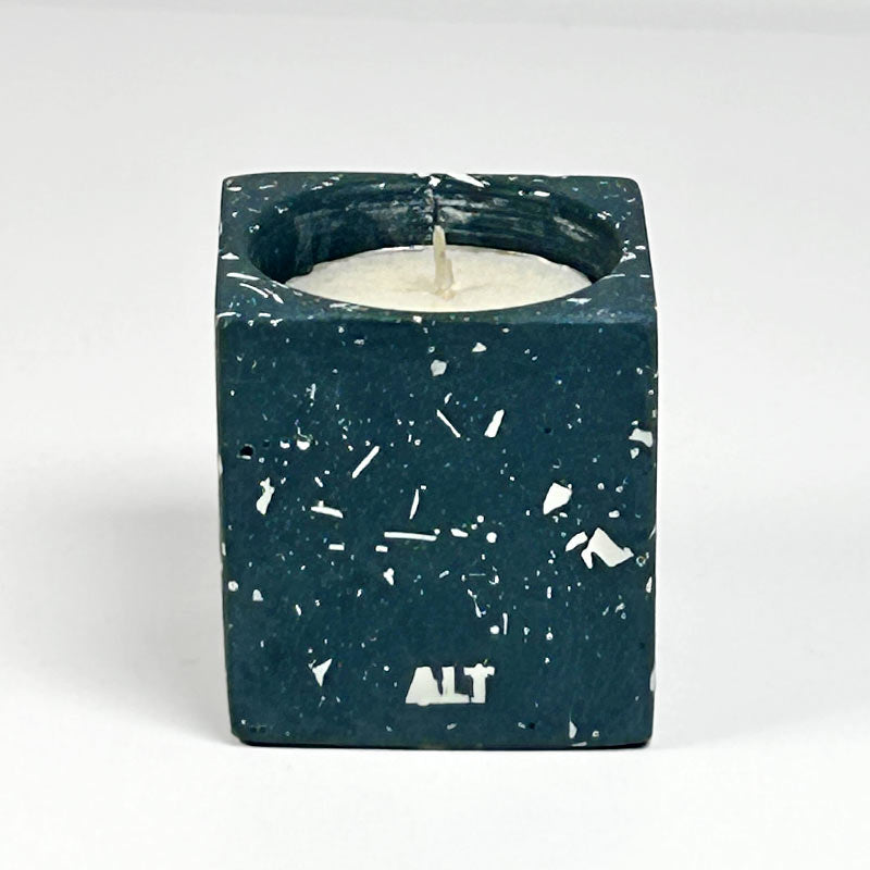 A rectangular navy candle holder with white terrazzo, containing a white tea light candle. The word 'ALT' is printed in white near the bottom front.