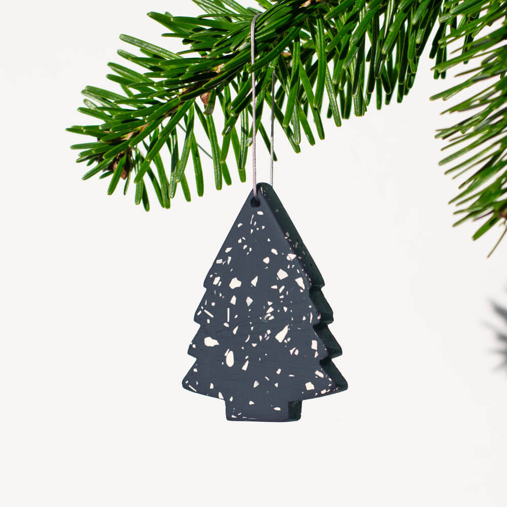 Navy terrazzo Christmas tree ornament hanging on a green branch against a white background