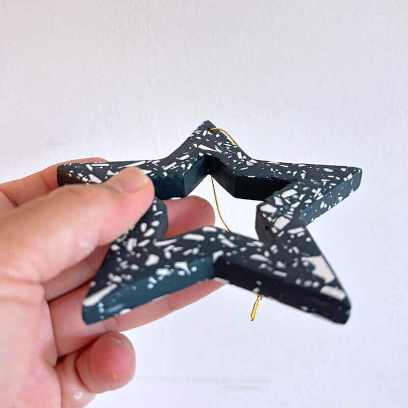 Hand holding a navy terrazzp star-shaped Christmas ornament against a white background