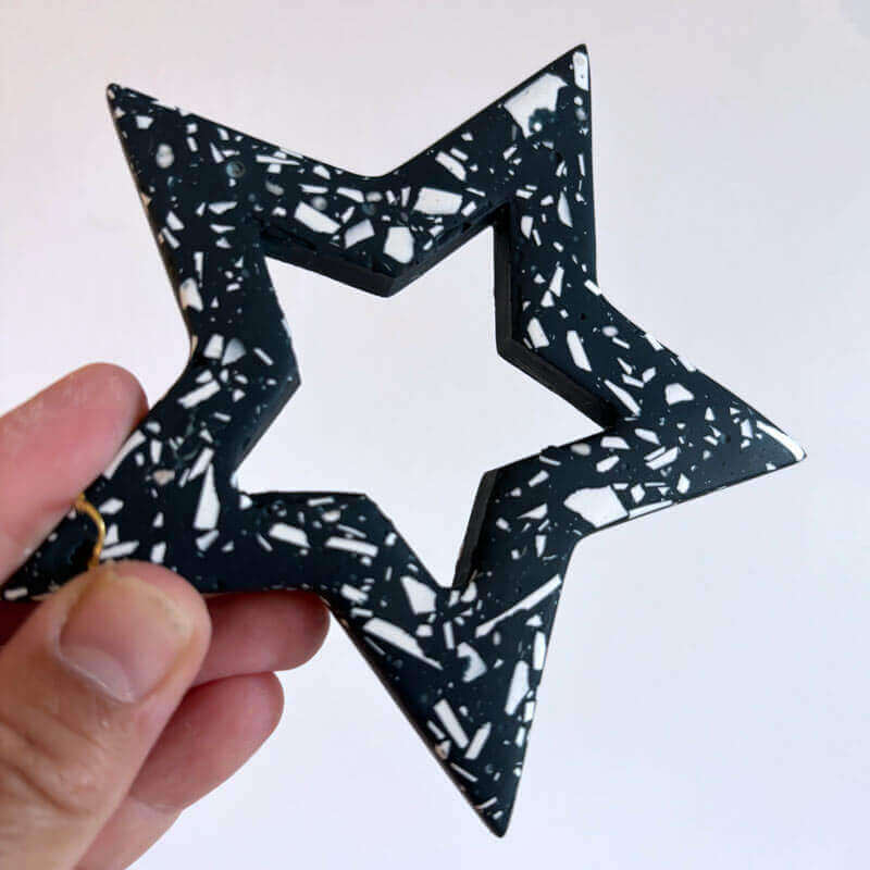 Hand holding a navy terrazzp star-shaped Christmas ornament against a white background