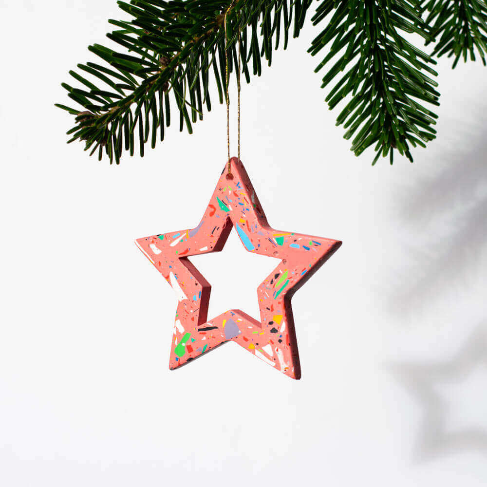 Pink with rainbow terrazzo star-shaped ornament hanging against a light purple background.