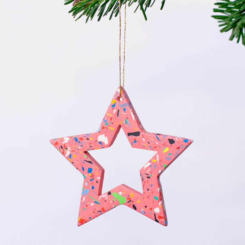 Pink with rainbow terrazzo star-shaped ornament hanging against a light purple background.