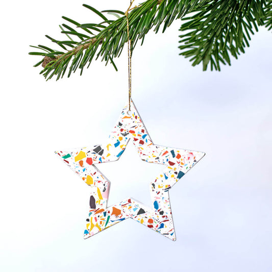 Star-shaped ornament with a colourful rainbow terrazzo hanging on a Christmas tree branch.