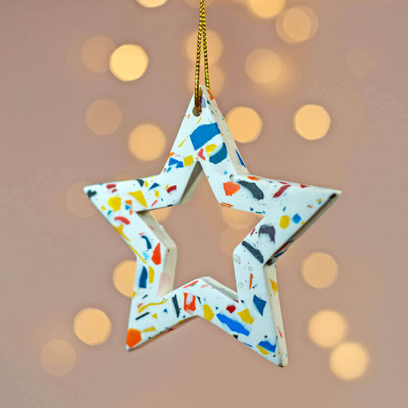 Colourful rainbow terrazzo star-shaped ornament with a gold chain against a bokeh light background