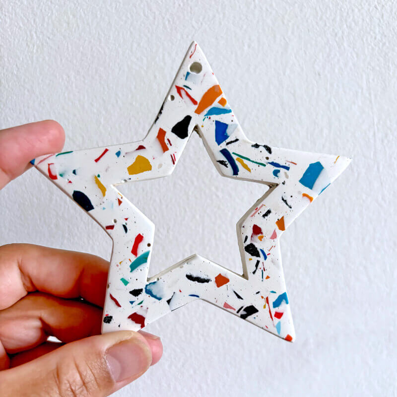 Rainbow terrazzo star-shaped Christmas ornament held by a hand against a white background