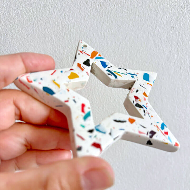 Rainbow terrazzo star-shaped Christmas ornament held by a hand against a white background