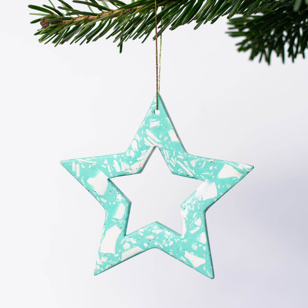 Star-shaped turquoise Christmas ornament with white terrazzo on a white background, hanging from a branch.