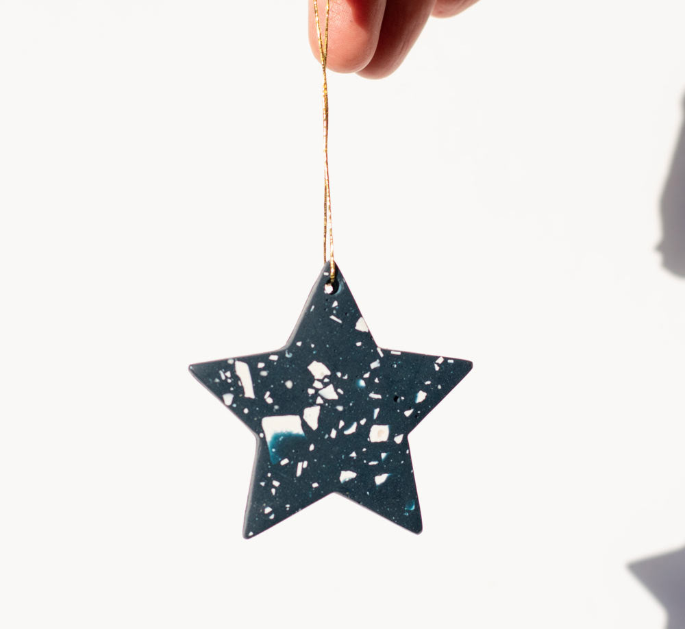 Star-shaped navy with white terrazzo Christmas decorative ornament held by a hand against a white background