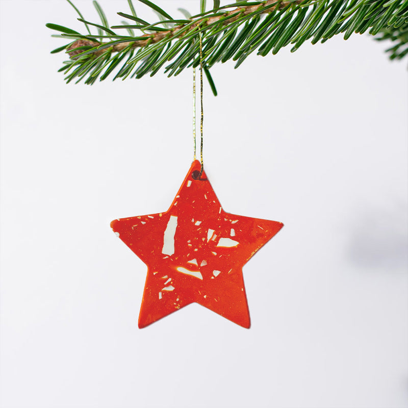 Star-shaped small Christmas ornament with orange terrazzo hanging from a branch.