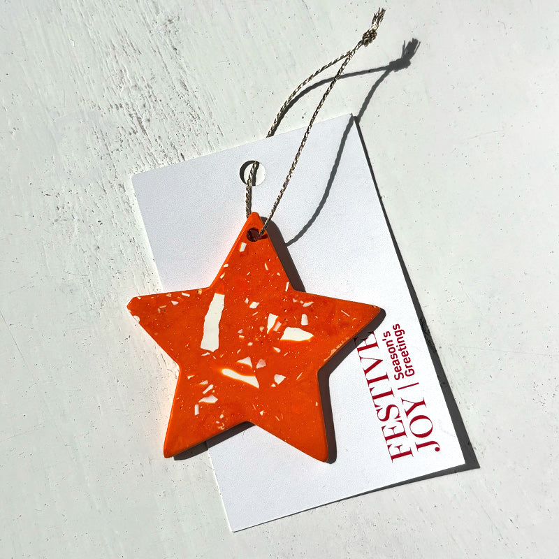 Orange terrazzo star-shaped ornament on a white card with Festive Joy red text on a white background