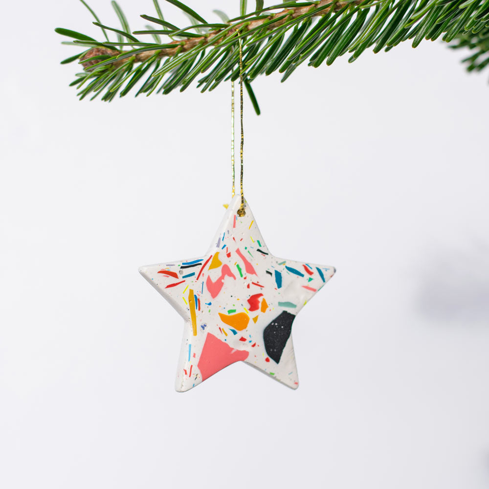 Star-shaped small Christmas ornament with rainbow confetti terrazzo hanging from a branch.