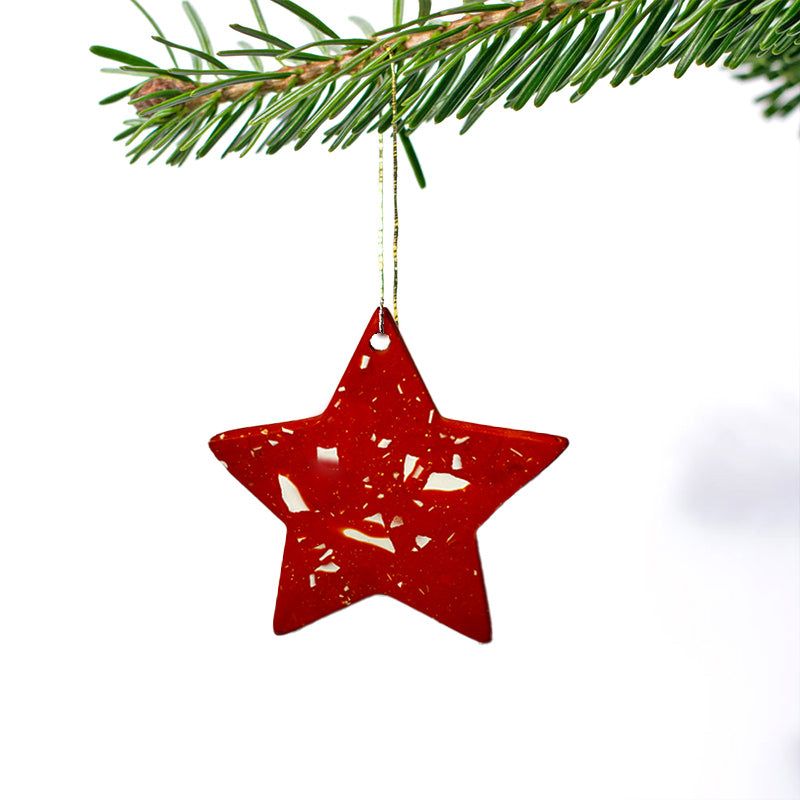 Red star-shaped Christmas ornament hanging from a branch on a white background