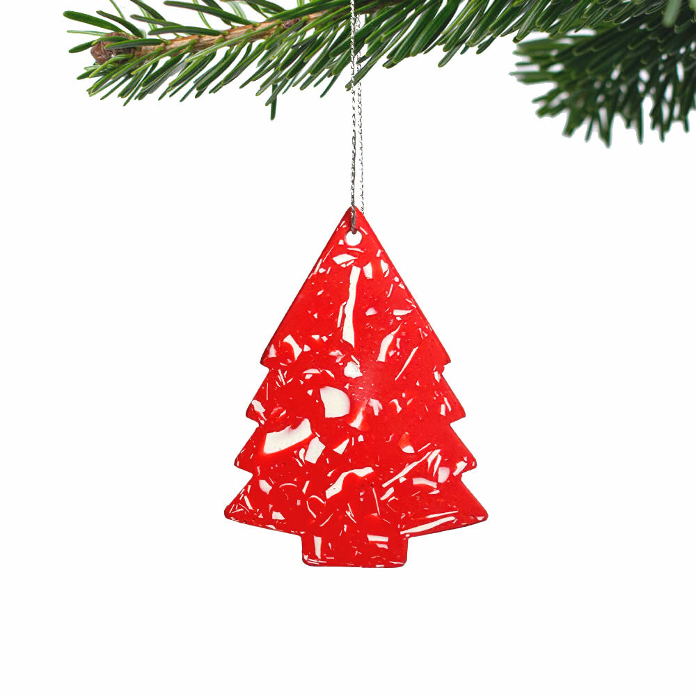 A red Christmas tree-shaped hanging ornament with a textured, marbled pattern, suspended by a thin silver string from a green pine branch against a white background.