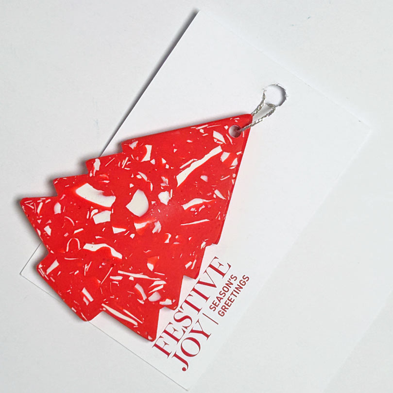 A red and white terrazzo Christmas tree-shaped ornament attached to a white greeting card that reads 'Festive Joy Season's Greetings'.
